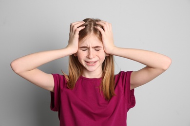 Photo of Teenage girl suffering from headache on grey background