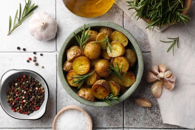 Photo of Flat lay composition with tasty baked potato and aromatic rosemary on light tiled table