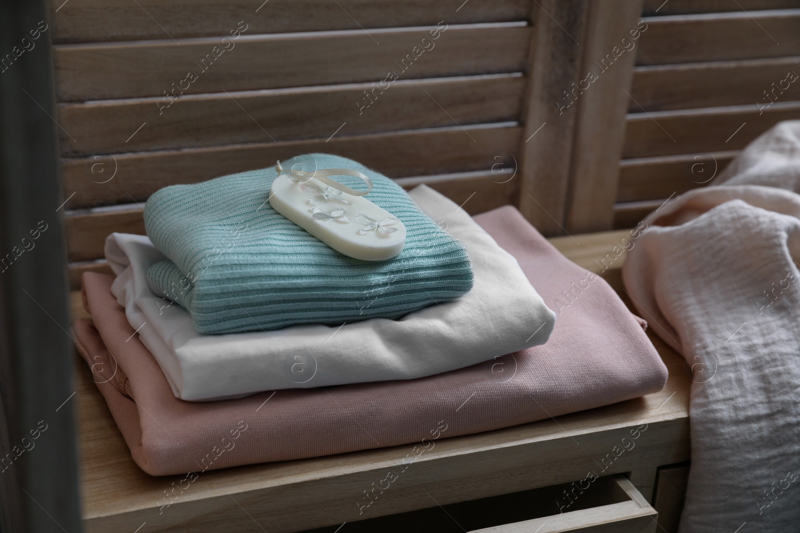 Photo of Beautiful scented wax sachet and stack of clothes on wooden dresser indoors