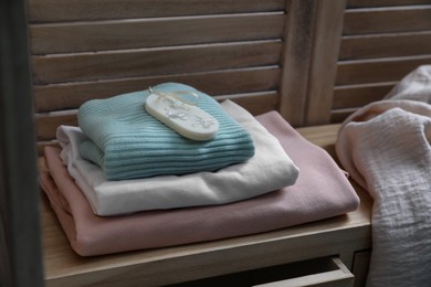 Beautiful scented wax sachet and stack of clothes on wooden dresser indoors