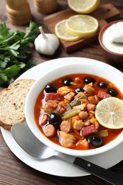 Photo of Meat solyanka soup with sausages, olives and vegetables served on wooden table, above view