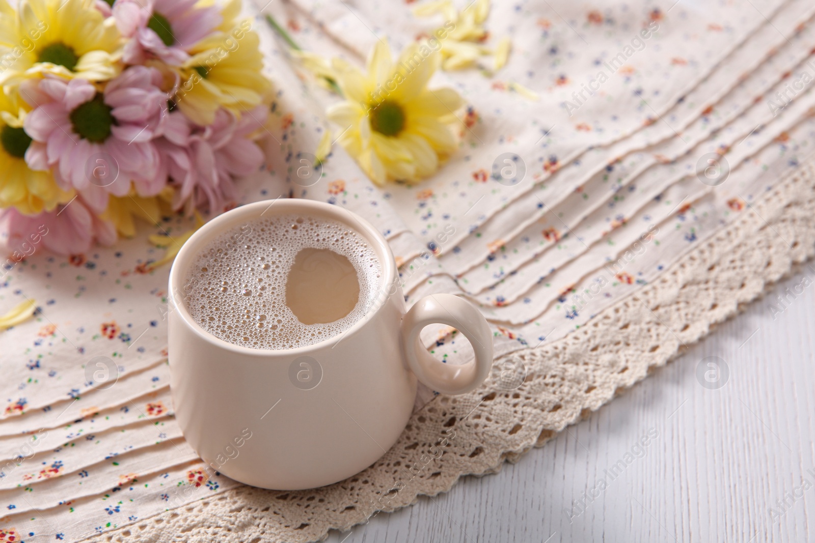 Photo of Cup of fresh coffee and beautiful bouquet on light beige printed cloth, space for text. Good morning