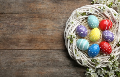 Photo of Flat lay composition with painted Easter eggs and blossoming branches on wooden background. Space for text