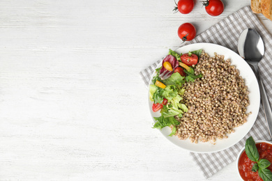 Tasty buckwheat porridge with salad on white wooden table, flat lay. Space for text