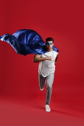 Photo of Man in superhero cape and mask running on red background
