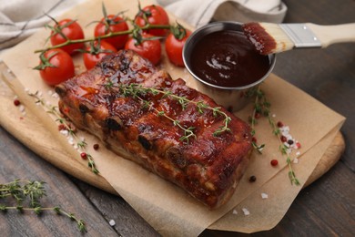 Photo of Tasty roasted pork ribs served with thyme, sauce and tomatoes on wooden table, closeup