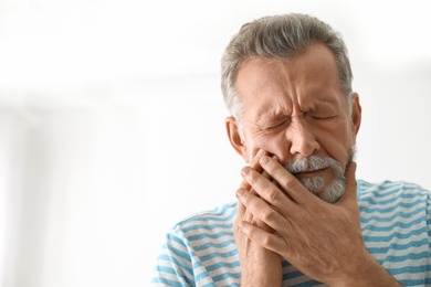 Photo of Mature man suffering from strong tooth pain on light background, space for text