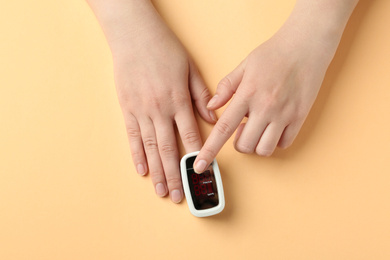 Photo of Woman using fingertip pulse oximeter on light orange background, top view