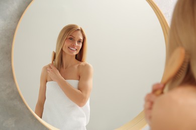 Photo of Beautiful woman brushing her hair near mirror in bathroom