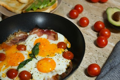 Fried with eggs, bacon and tomatoes in frying pan near ingredients on wooden table, closeup. Tasty breakfast