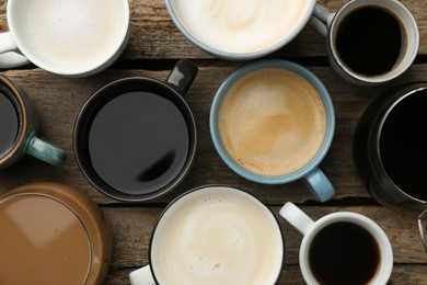 Different coffee drinks in cups on wooden table, flat lay