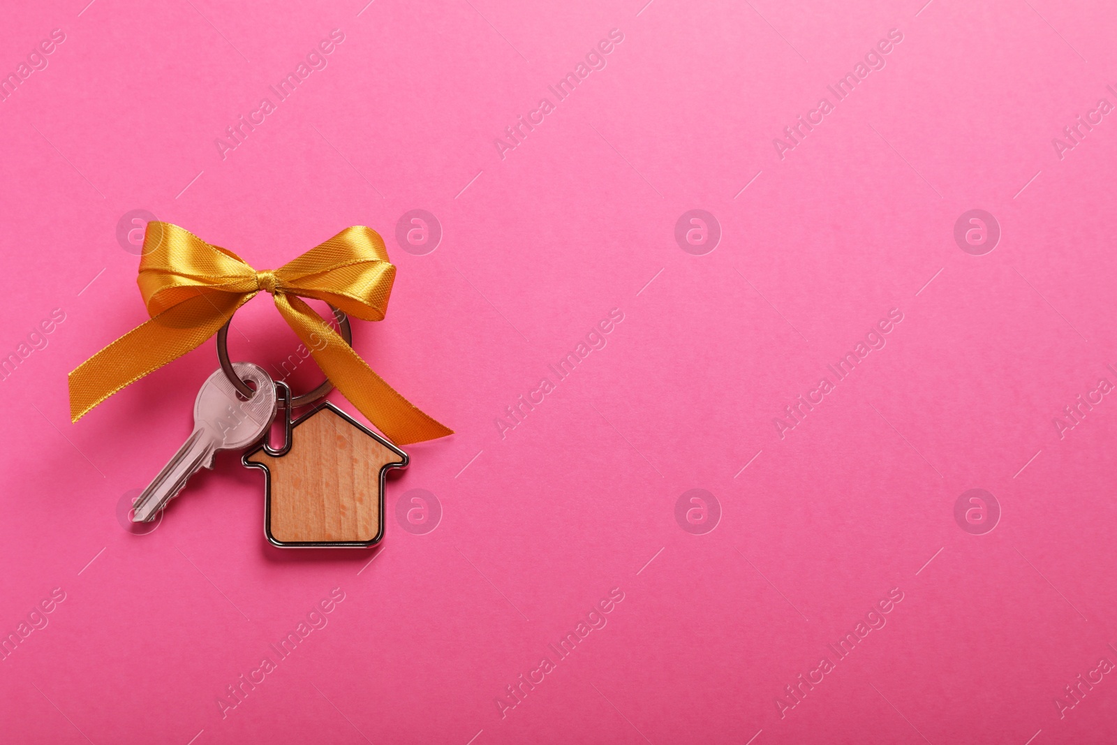 Photo of Key with trinket in shape of house and bow on pink background, top view. Space for text. Housewarming party