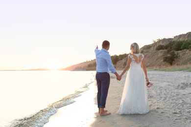 Photo of Wedding couple holding hands at sunset on beach. Space for text
