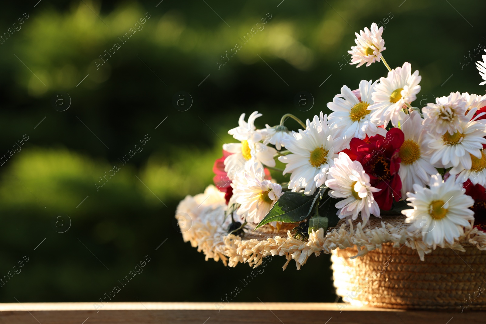 Photo of Beautiful wild flowers in wicker basket on wooden table against blurred background, closeup. Space for text