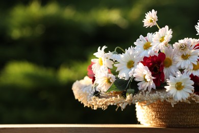 Beautiful wild flowers in wicker basket on wooden table against blurred background, closeup. Space for text