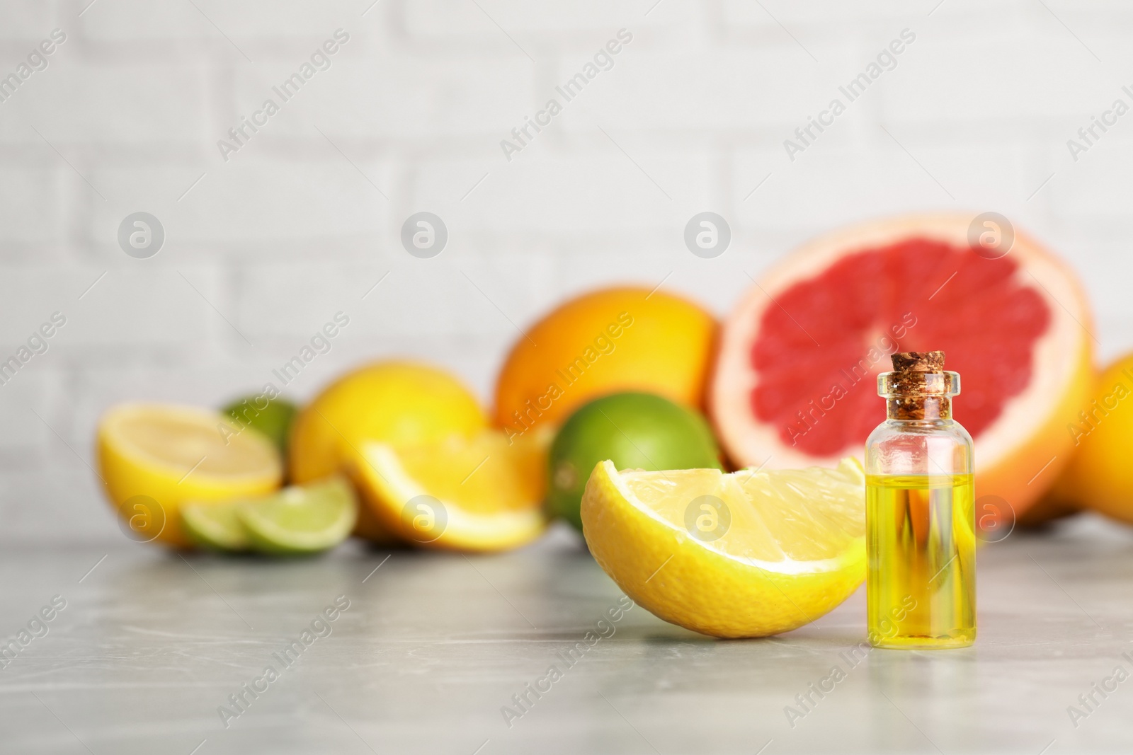 Photo of Bottle of essential oil with different citrus fruits on grey marble table. Space for text