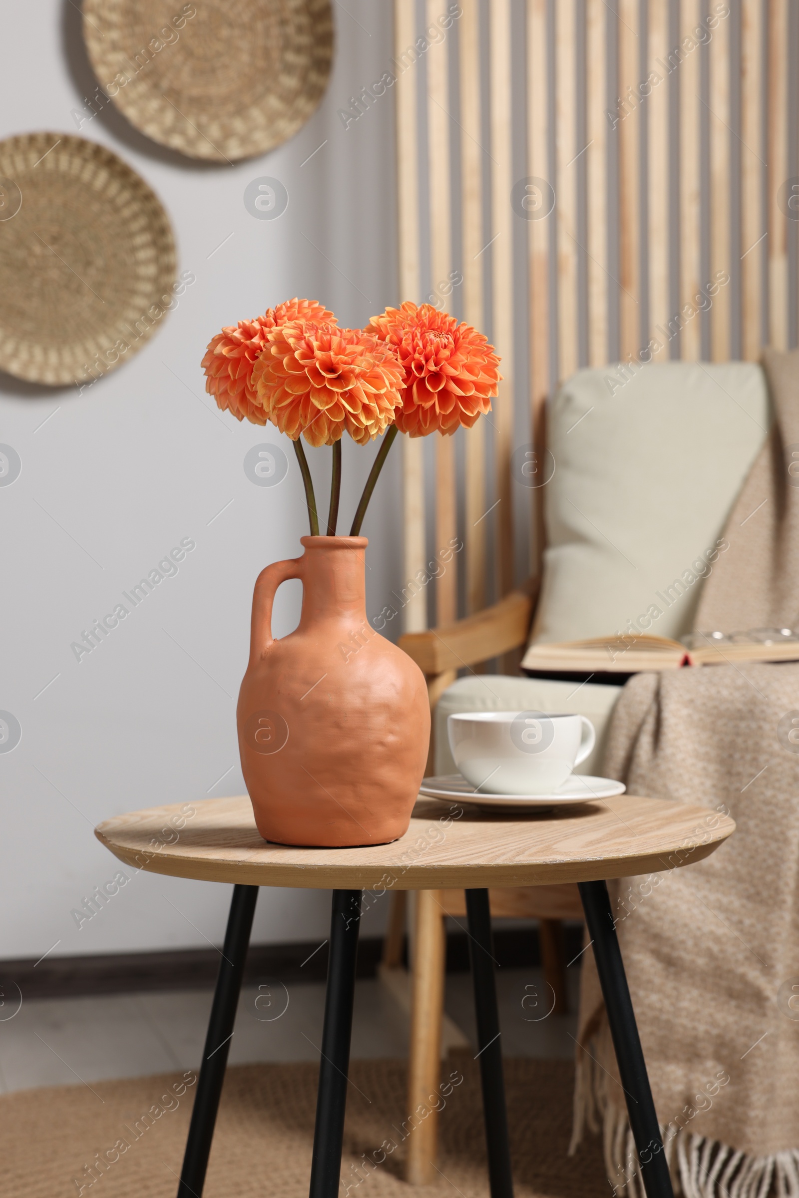 Photo of Ceramic vase with beautiful flowers on coffee table near armchair indoors