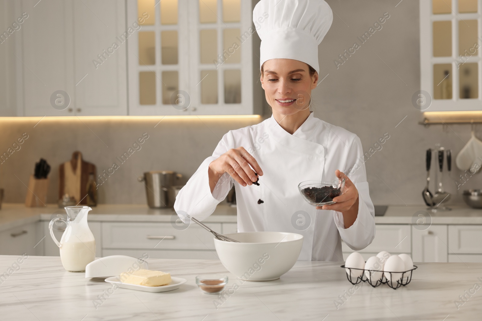 Photo of Professional chef adding raisins into dough at white marble table in kitchen