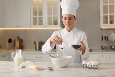 Photo of Professional chef adding raisins into dough at white marble table in kitchen