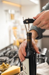 Man opening wine bottle with corkscrew indoors, closeup