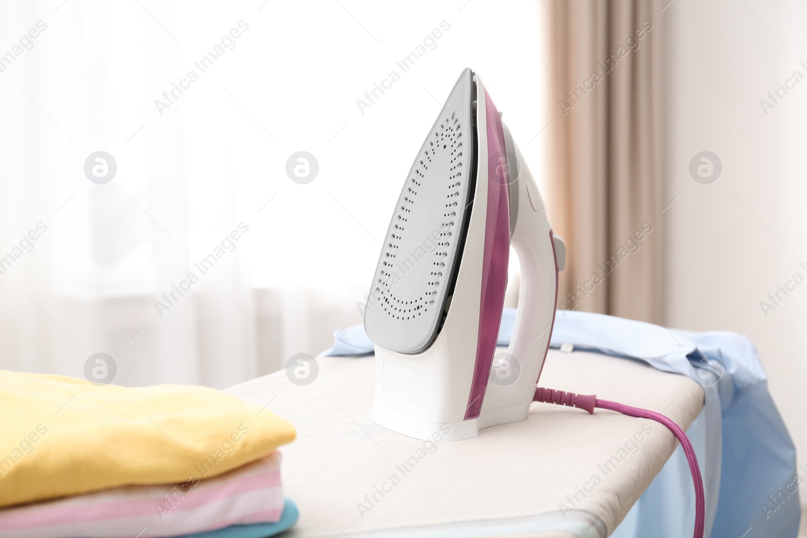 Photo of Board with modern iron and clean clothes indoors. Laundry day