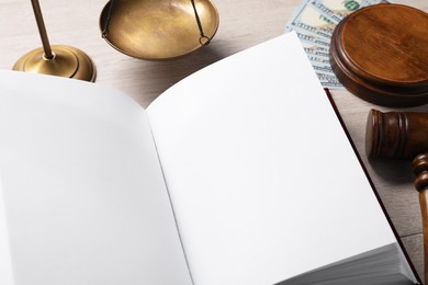 Tax law. Open book, gavel, dollar banknotes and scales on wooden table, closeup