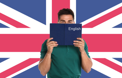Image of Handsome young man reading book and flag of Great Britain on wall. Learning English