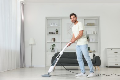Photo of Happy man cleaning floor with steam mop at home