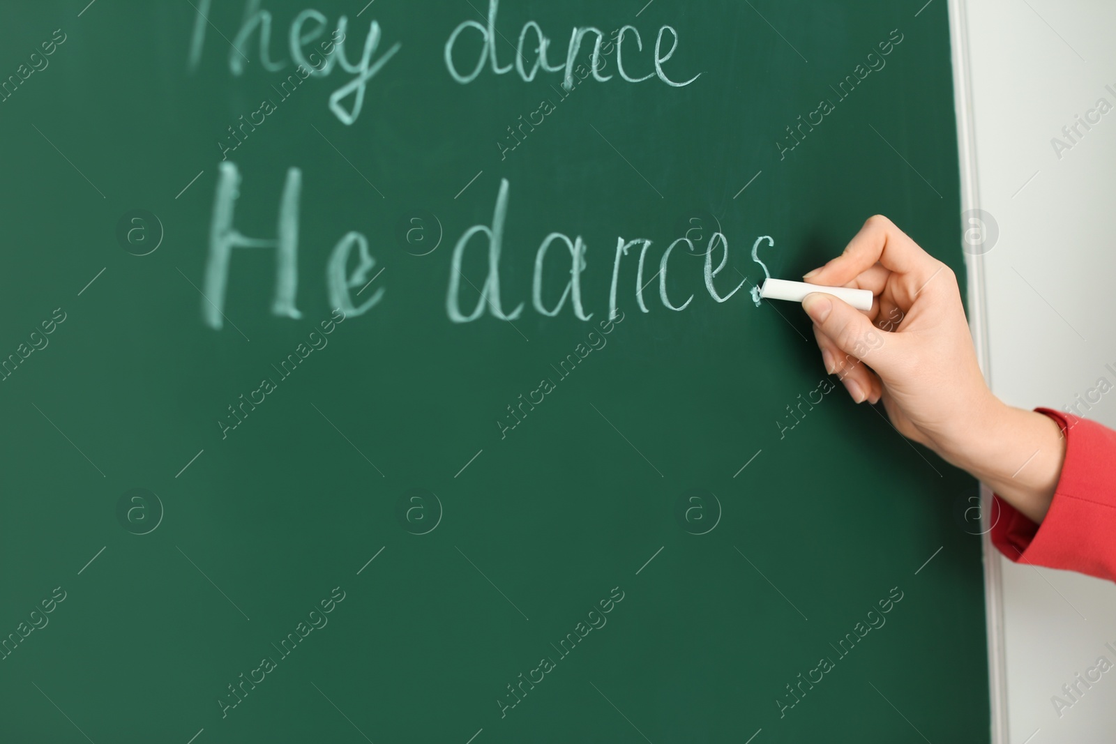 Photo of English teacher writing on green chalkboard at lesson, closeup