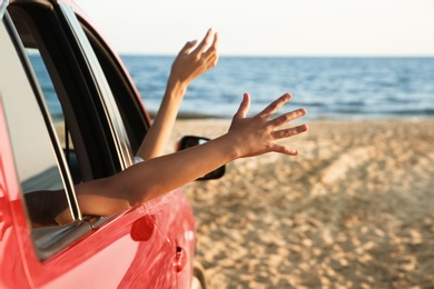 Woman and her daughter waving from car on beach, closeup. Summer trip