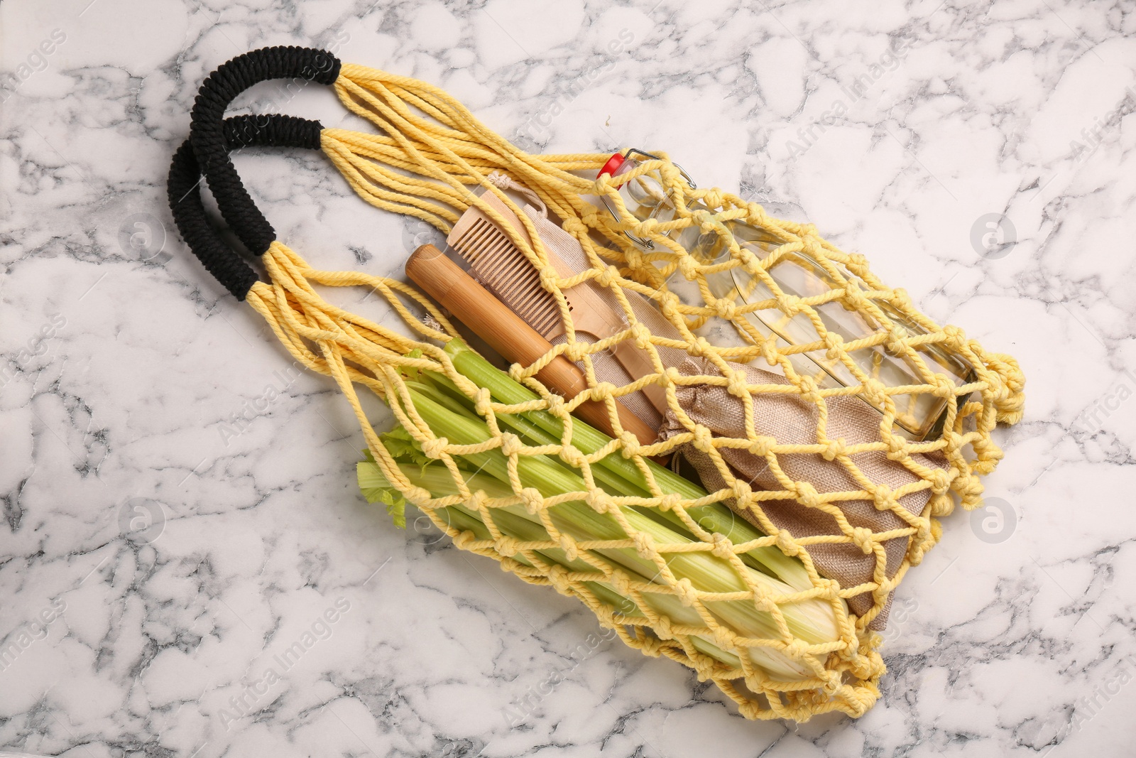 Photo of Net bag with different items on white marble table, top view. Conscious consumption