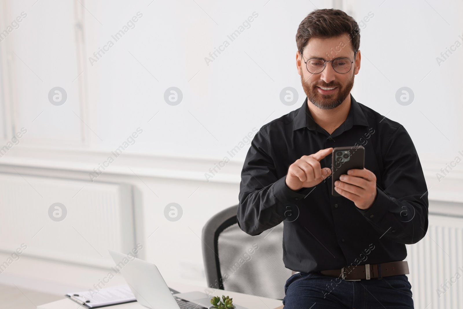 Photo of Smiling man using smartphone in office. Space for text