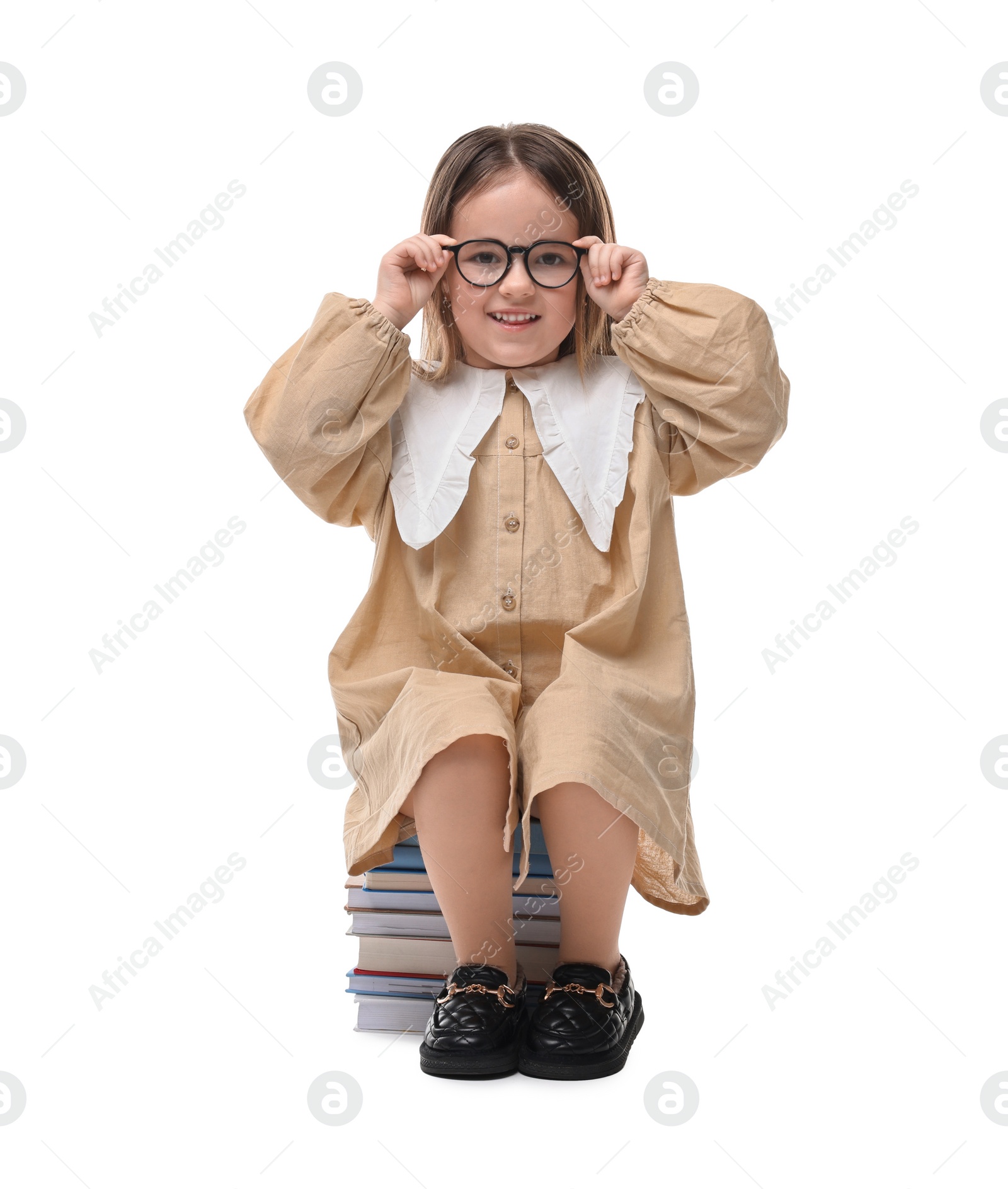 Photo of Cute little girl in glasses sitting on stack of books against white background