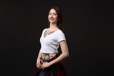 Photo of Portrait of smiling tattooed woman on black background. Space for text