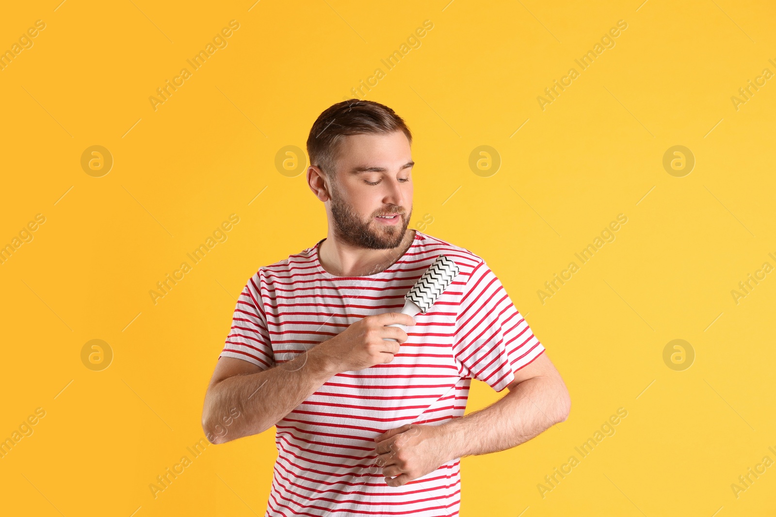 Photo of Young man cleaning clothes with lint roller on yellow background