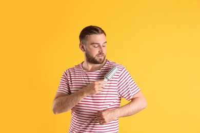 Photo of Young man cleaning clothes with lint roller on yellow background