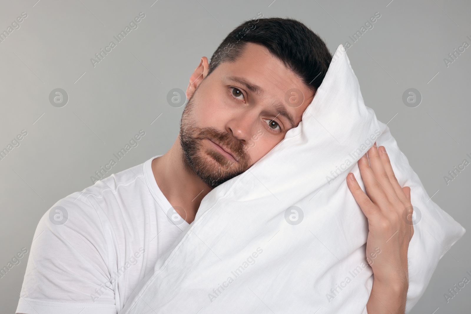 Photo of Sleepy man with pillow on grey background. Insomnia problem