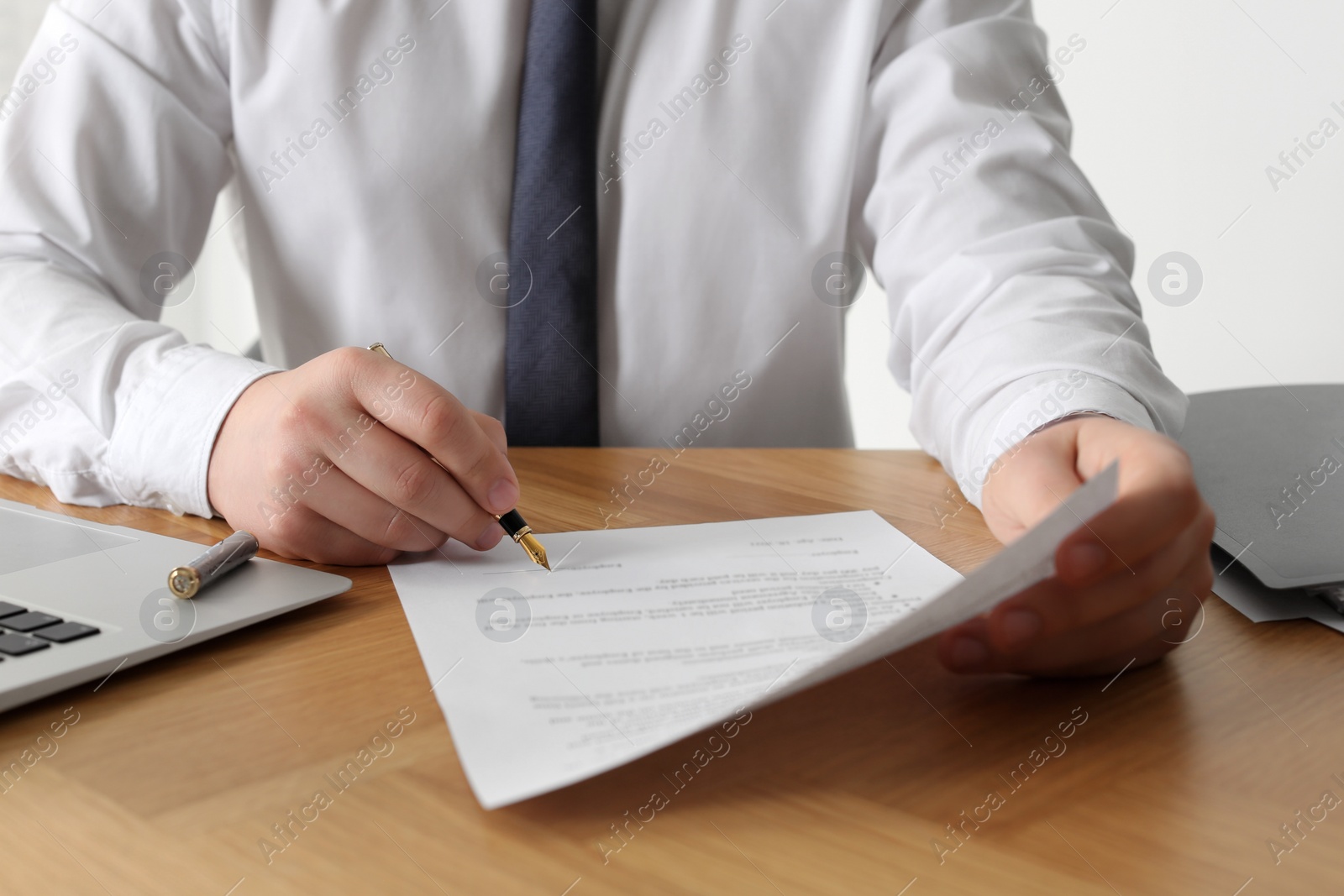 Photo of Notary signing document at wooden table, closeup