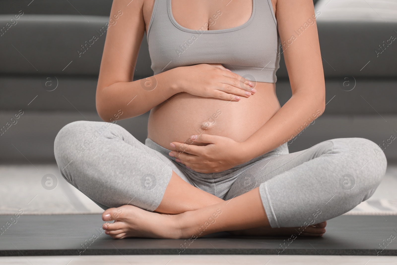 Photo of Pregnant woman sitting on yoga mat at home, closeup