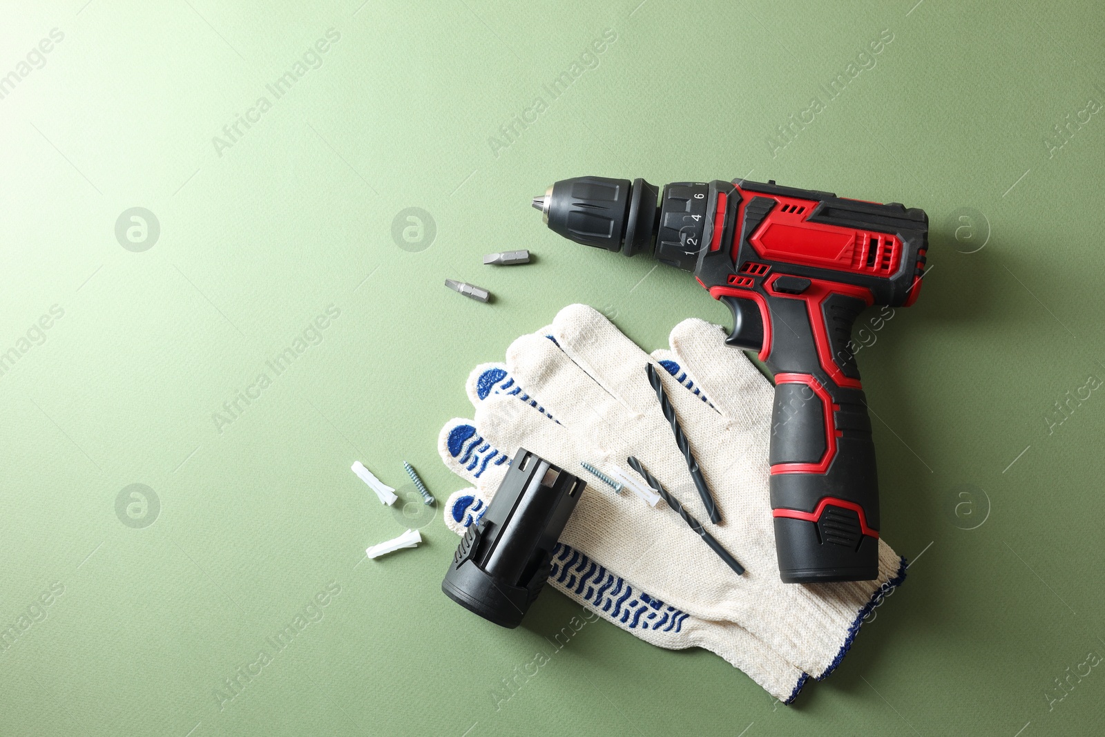 Photo of Electric screwdriver, gloves and accessories on pale green background, flat lay