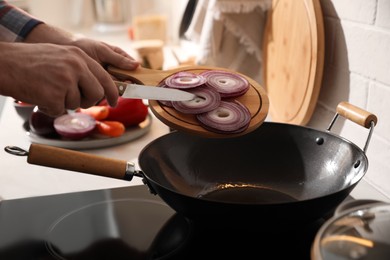 Photo of Man pouring onion slices into frying pan, closeup