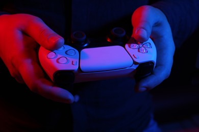 Photo of Man using wireless game controller on dark background in neon lights, closeup