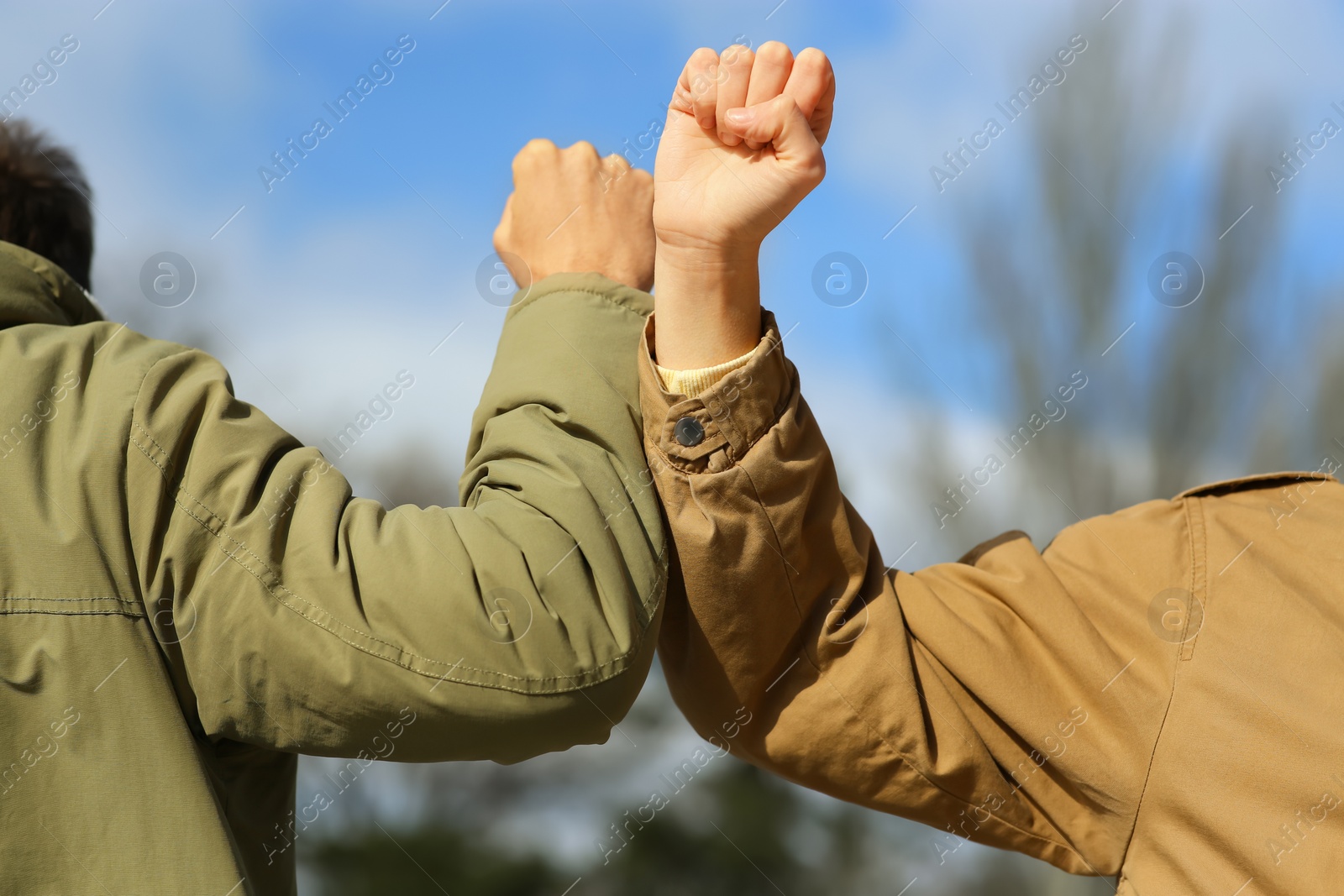 Photo of People greeting each other by bumping elbows instead of handshake outdoors, closeup
