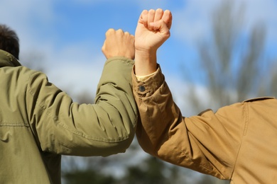 People greeting each other by bumping elbows instead of handshake outdoors, closeup