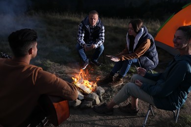 Photo of Group of friends gathering around bonfire at camping site in evening