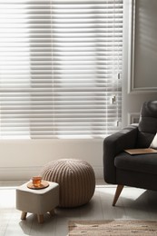 Tray with cup of tea on stylish ottoman and comfortable pouf in room