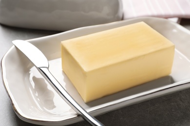 Dish with fresh butter and knife on table, closeup