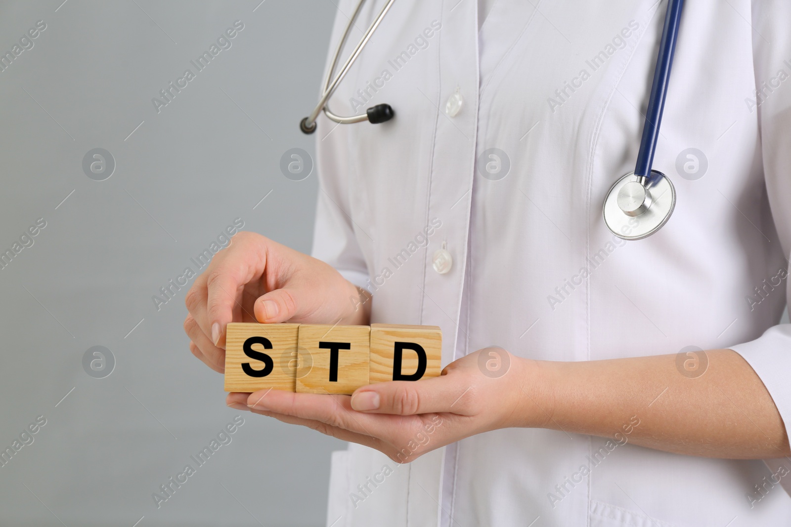 Photo of Doctor holding wooden cubes with abbreviation STD on grey background, closeup