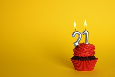Photo of Delicious cupcake with number shaped candles on yellow background, space for text. Coming of age party - 21th birthday