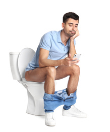 Photo of Emotional man with smartphone sitting on toilet bowl, white background